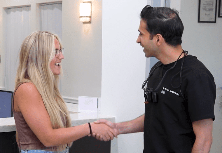 Woman smiling while shaking hands with her dentist in The Woodlands dental office