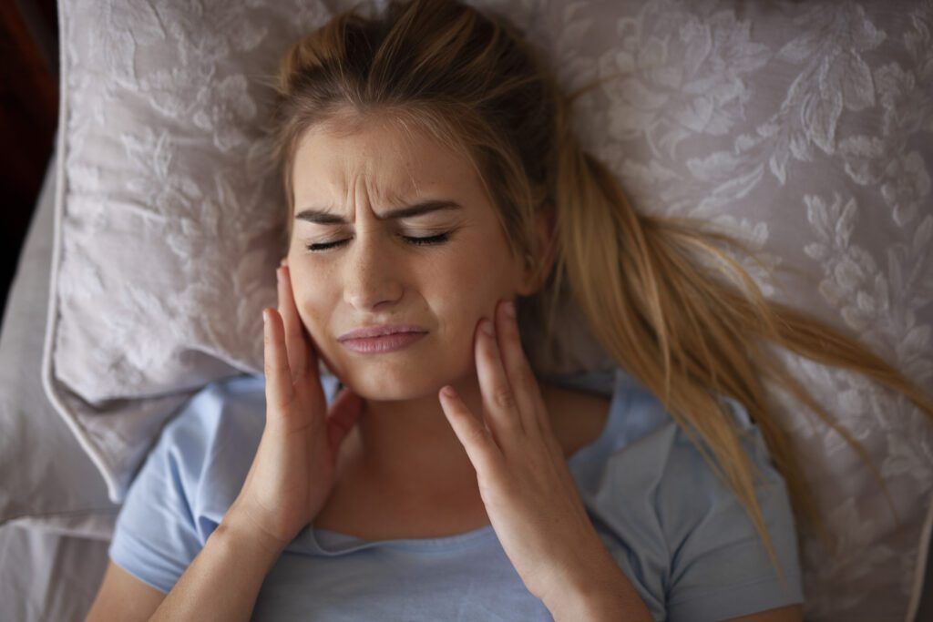 Woman holding the sides of her jaw in pain before T M J treatment in The Woodlands