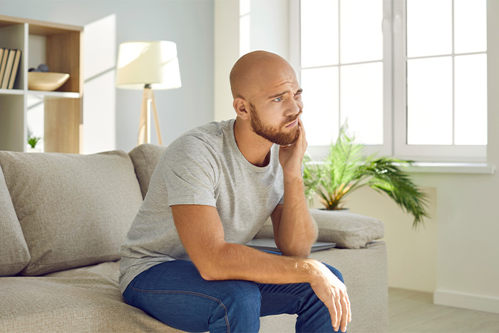 Man with beard sitting on couch with tooth pain