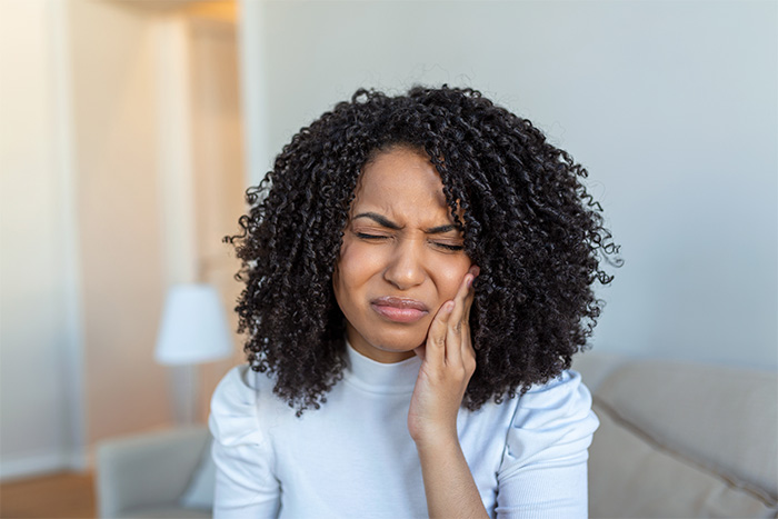 Woman in living room rubbing jaw in pain