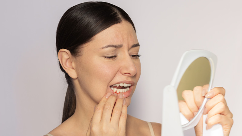 Concerned woman looking at her gums in hand mirror