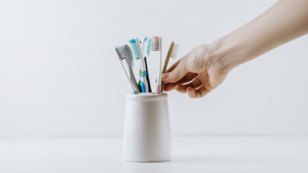 A person holding a vase filled with multiple toothbrushes, symbolizing dental care and oral hygiene.