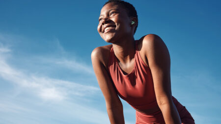 Smiling woman wearing a red tank top leans forward confidently against a blue sky backdrop, conveying energy and positivity.