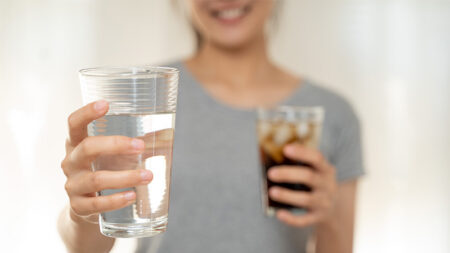 A person holding a glass of water and a glass of soda.