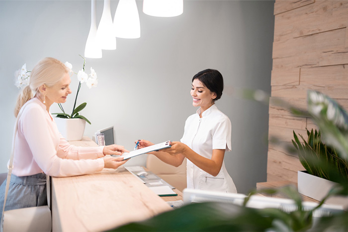 Smiling dental receptionist handing patient form.