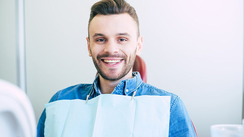 Man in denim jacket sitting in dental chair and smiling.