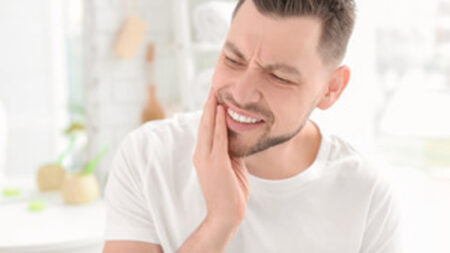 Man in white shirt rubbing his jaw in pain.