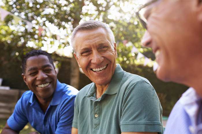 Three men smiling and laughing together outdoors under bright sunlight.